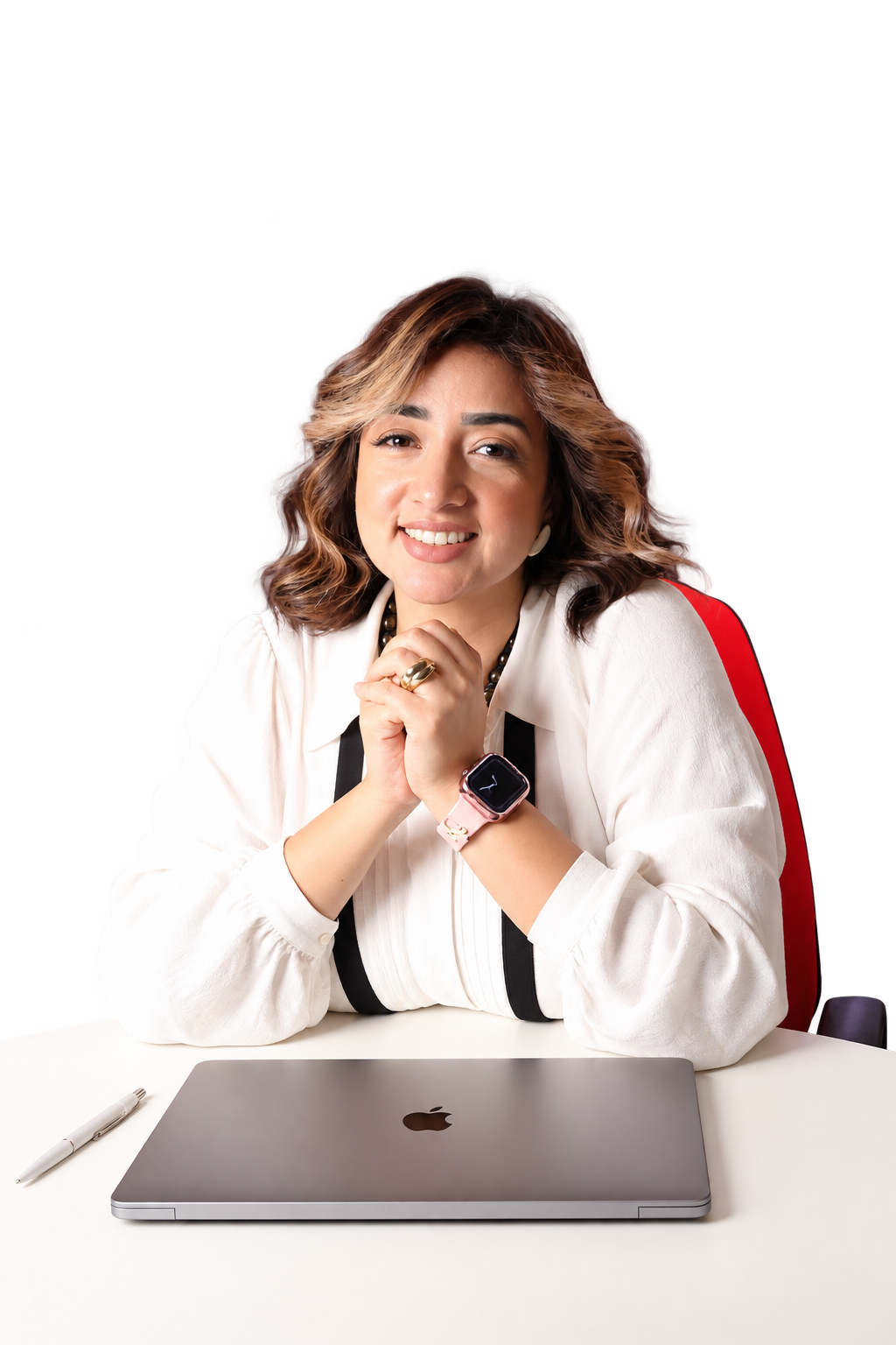 Mai Sami seated at her white desk with a closed laptop and pen, smiling with her elbows resting on the tabletop
